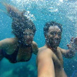 An underwater photo of two people smiling and waving happily with bubbles everywhere